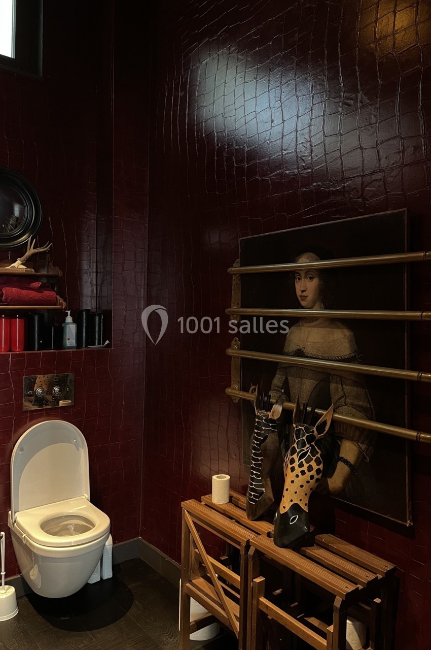Salle de bain avec murs rouge foncé, toilette blanche, étagères en bois et tableau décoratif.