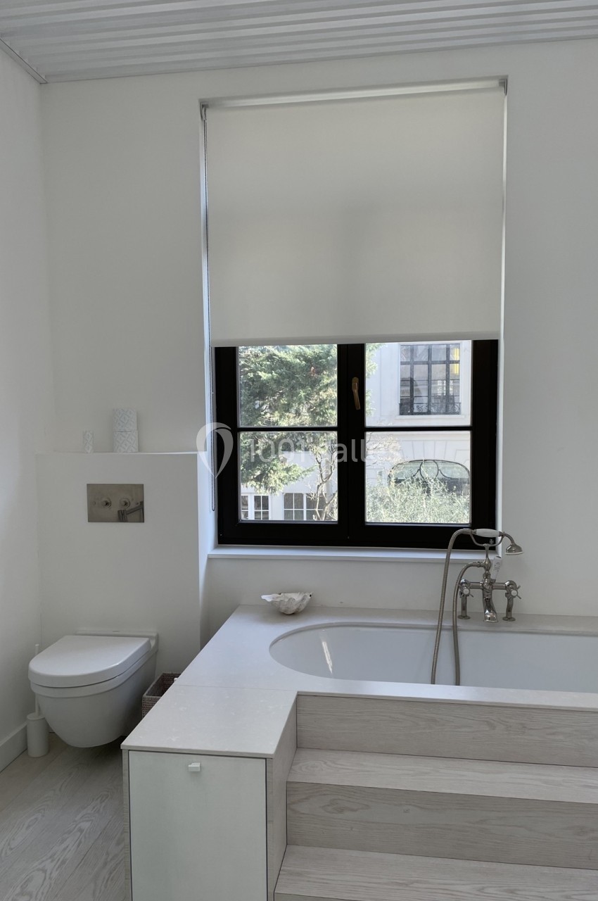 Salle de bain lumineuse avec baignoire, toilettes suspendues et fenêtre donnant sur un jardin.