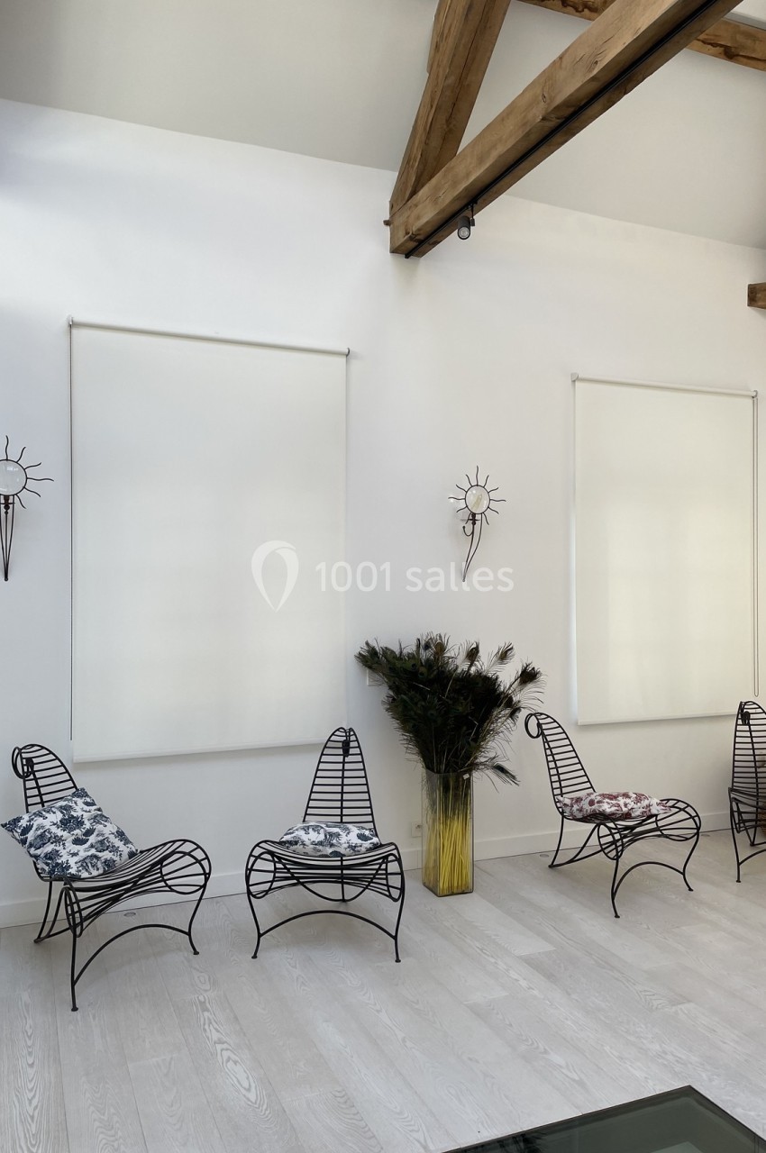 Quatre fauteuils en métal noir avec coussins, disposés dans une pièce lumineuse aux murs blancs et poutres apparentes.