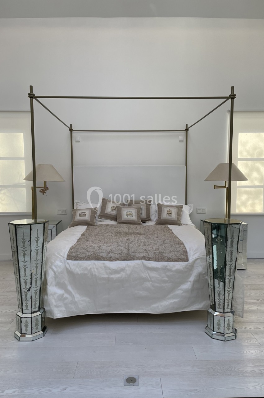 Lit à baldaquin moderne avec linge beige et blanc, encadré par deux lampes sur des tables de chevet en miroir.