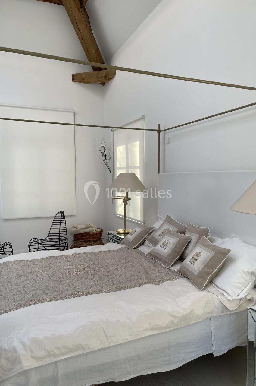 Lit à baldaquin dans une chambre lumineuse avec murs blancs, poutres apparentes et mobilier épuré.
