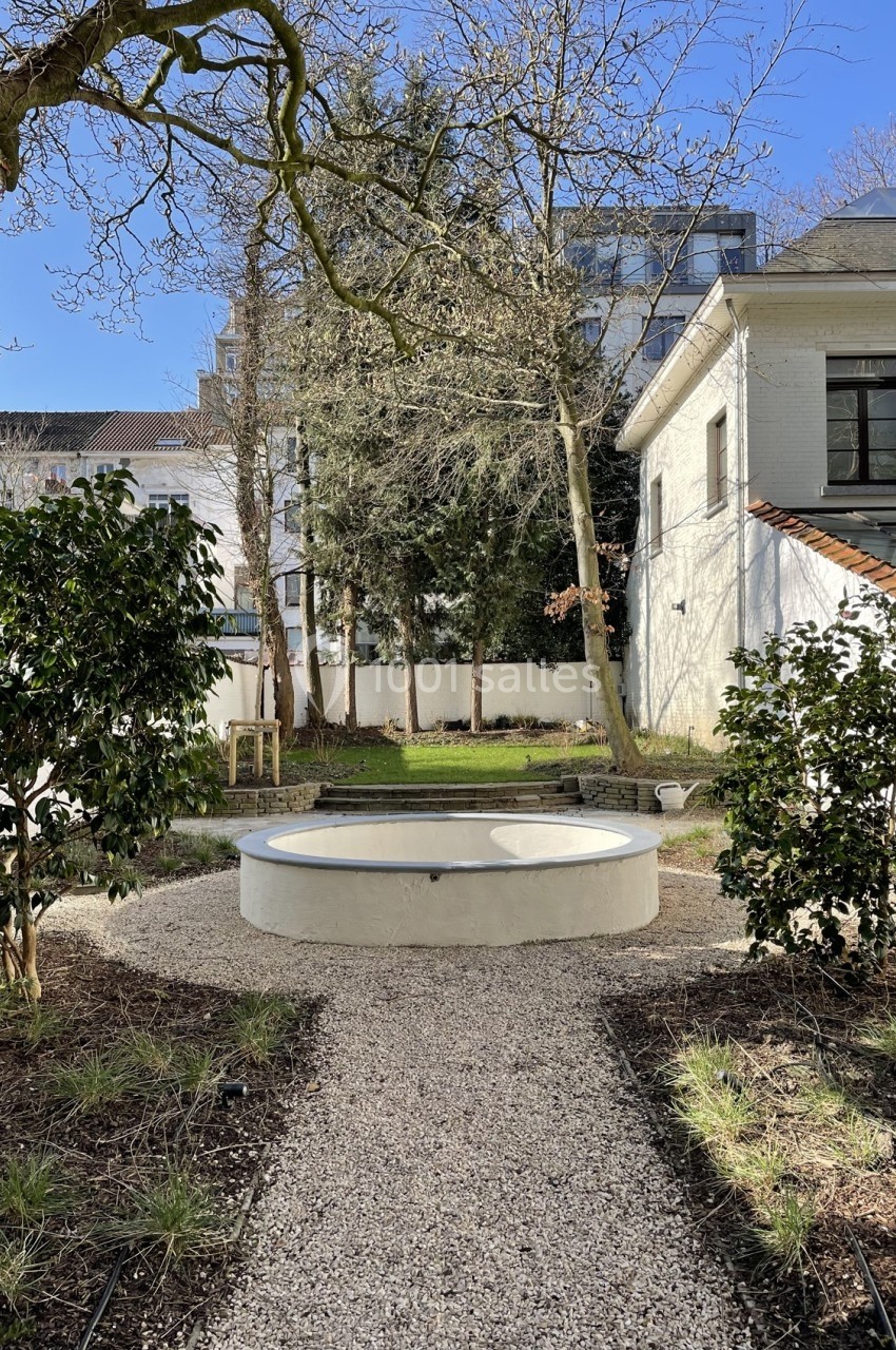 Petit jardin avec un chemin de gravier menant à une fontaine circulaire entourée de végétation et d'arbres.