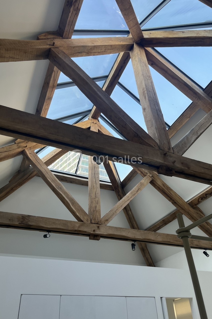 Charpente en bois apparente sous un plafond incliné avec une grande verrière laissant entrer la lumière naturelle.
