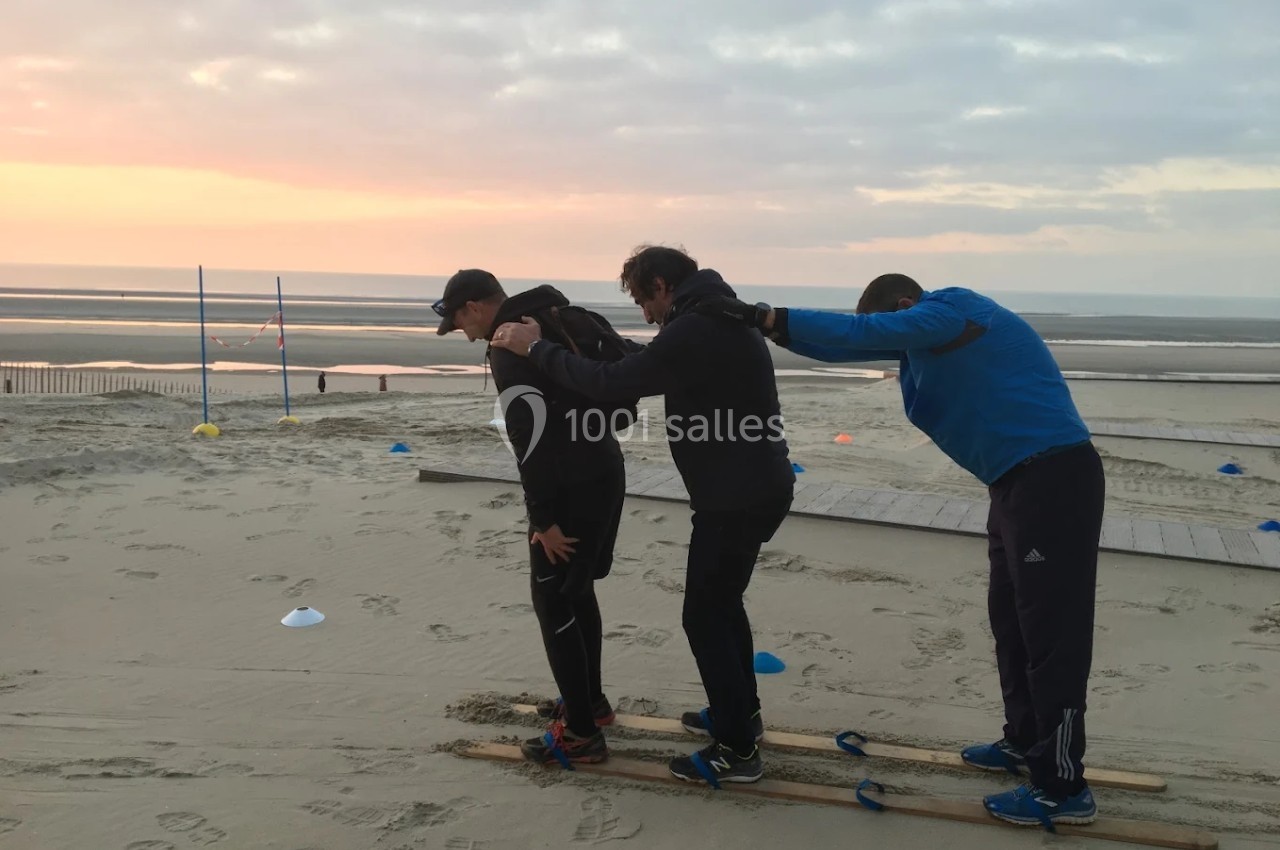 Trois personnes coopèrent sur des skis en bois sur une plage au lever du soleil.