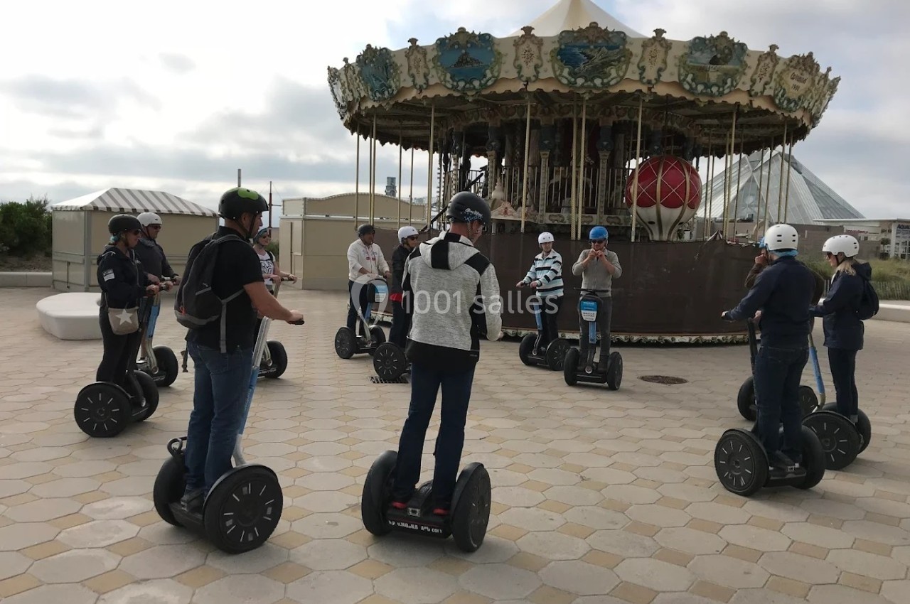 Groupe de personnes en gyropodes rassemblées devant un carrousel sur une place pavée.