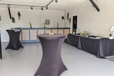 Miniature Location salle Saint-Guyomard (Morbihan) - Domaine de Ker Léon #23 Espace extérieur avec tables hautes noires sur une pelouse, devant un bâtiment vitré et un comptoir en bois.