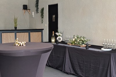 Miniature Location salle Saint-Guyomard (Morbihan) - Domaine de Ker Léon #25 Espace extérieur avec tables hautes noires sur une pelouse, devant un bâtiment vitré et un comptoir en bois.
