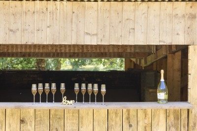 Miniature Location salle Saint-Guyomard (Morbihan) - Domaine de Ker Léon #68 Espace extérieur avec tables hautes noires sur une pelouse, devant un bâtiment vitré et un comptoir en bois.