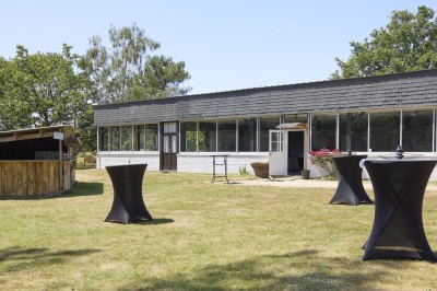 Miniature Location salle Saint-Guyomard (Morbihan) - Domaine de Ker Léon #93 Espace extérieur avec tables hautes noires sur une pelouse, devant un bâtiment vitré et un comptoir en bois.