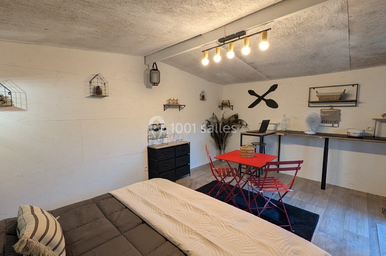 Chambre aménagée avec lit, table rouge et chaises, décorations murales et éclairage suspendu dans un style chaleureux.