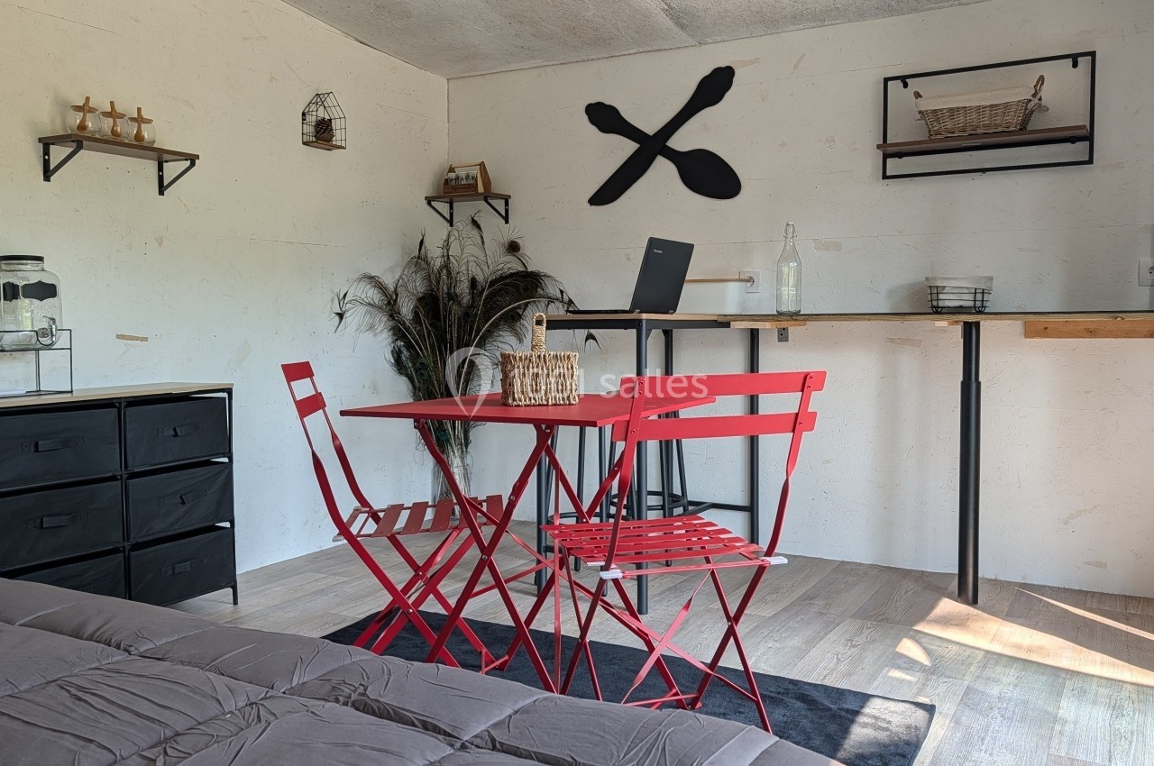 Salle aménagée avec table et chaises rouges, bureau avec ordinateur portable, étagères murales et décoration minimaliste.