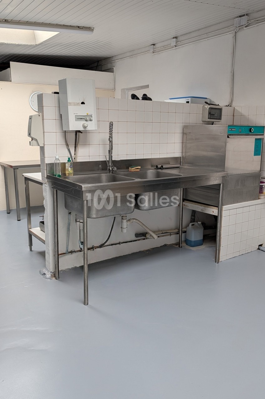 Cuisine professionnelle équipée d'un plan de travail inox avec double évier, chauffe-eau et réfrigérateur.