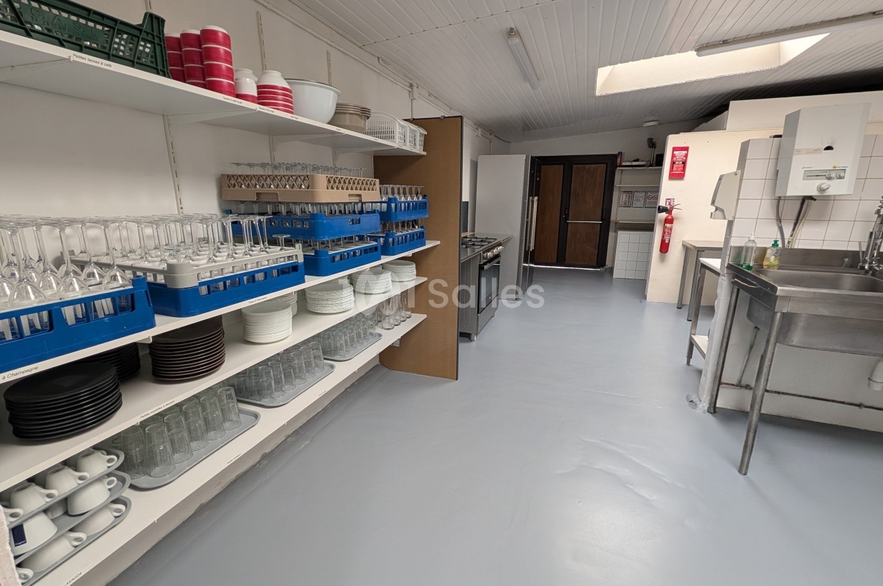 Cuisine professionnelle avec étagères de vaisselle, verres, assiettes et équipement inox - plan de travail dégagé.