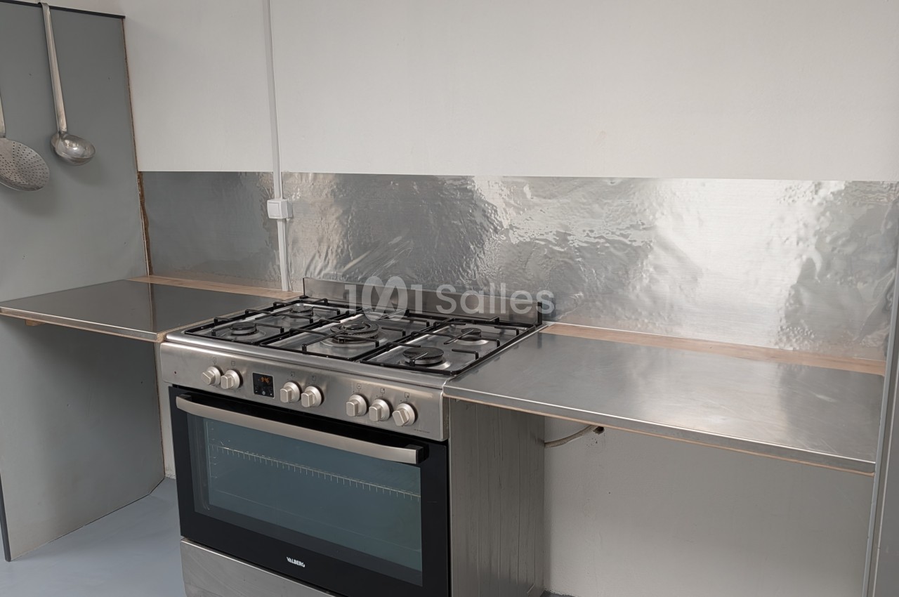 Cuisinette équipée d'une plaque de cuisson gaz, four intégré et plan de travail inox dans un espace blanc et gris.