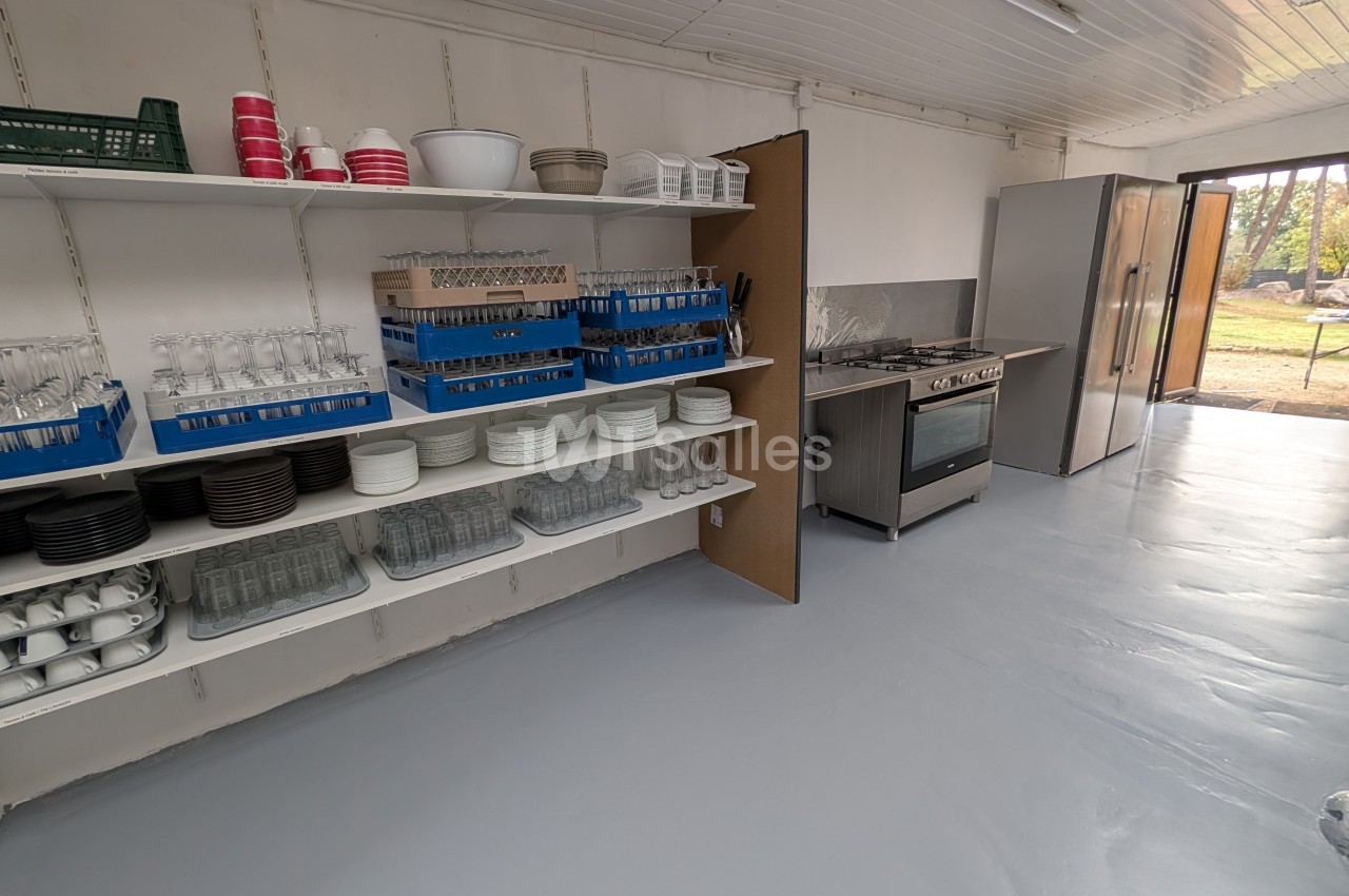 Cuisine professionnelle équipée avec étagères de vaisselle, bacs à glaçons bleus, appareils inox et vue sur l'extérieur.