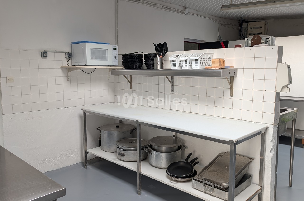 Cuisine professionnelle avec plan de travail inox, étagères murales et rangements, équipée de casseroles et ustensiles.