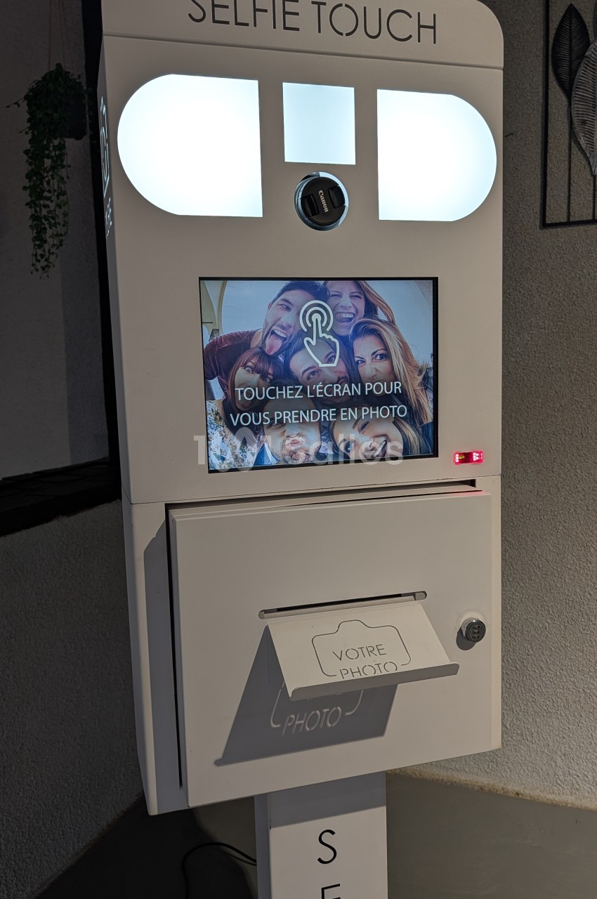 Photobooth blanc avec écrans LED, miroirs et bac à photos pour animations d'événements.
