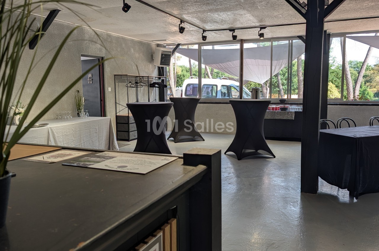 Salle intérieure avec tables hautes noires, comptoir blanc, grandes baies vitrées et éclairage par projecteurs.