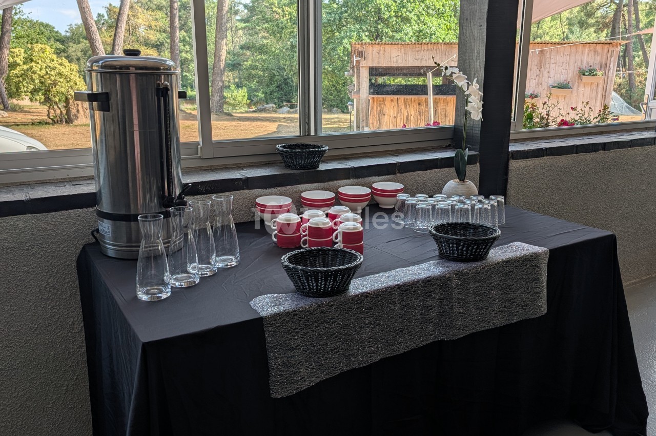 Table dressée avec service à café rouge et blanc, verres et paniers - baie vitrée ouvrant sur jardin boisé.