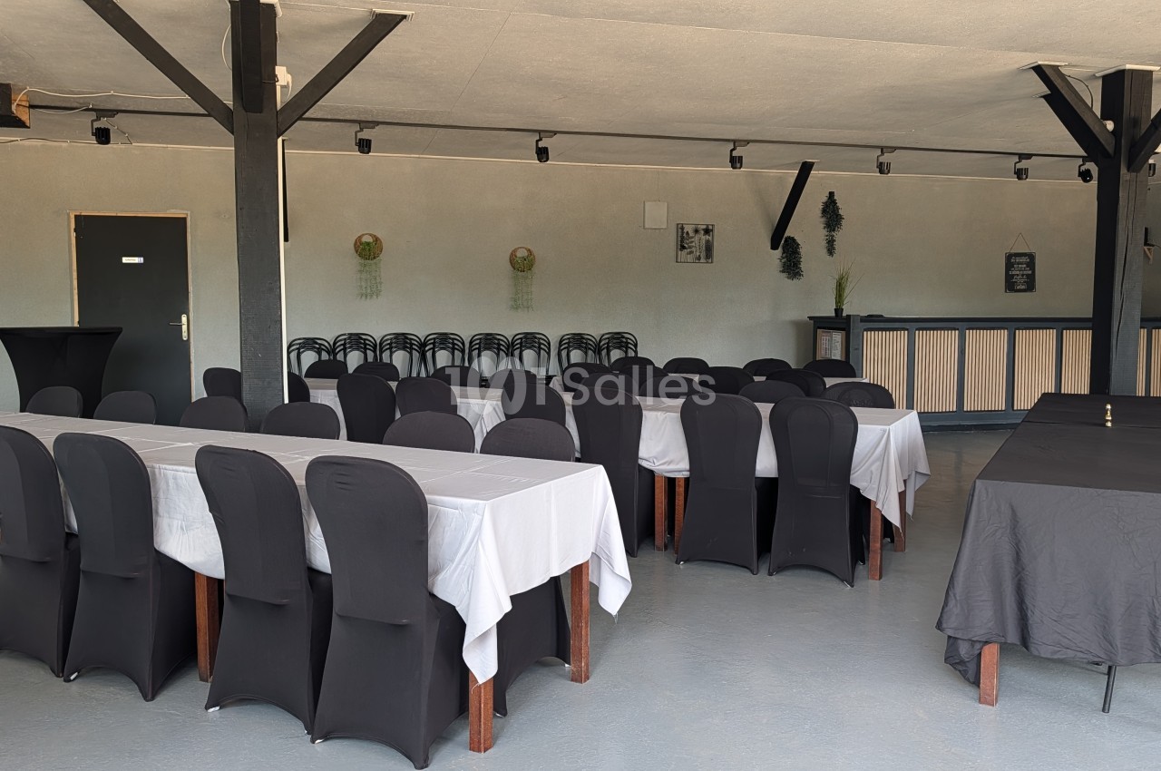 Salle intérieure avec tables rondes dressées, chaises noires, nappes blanches et décoration murale - capacité environ 80 places.