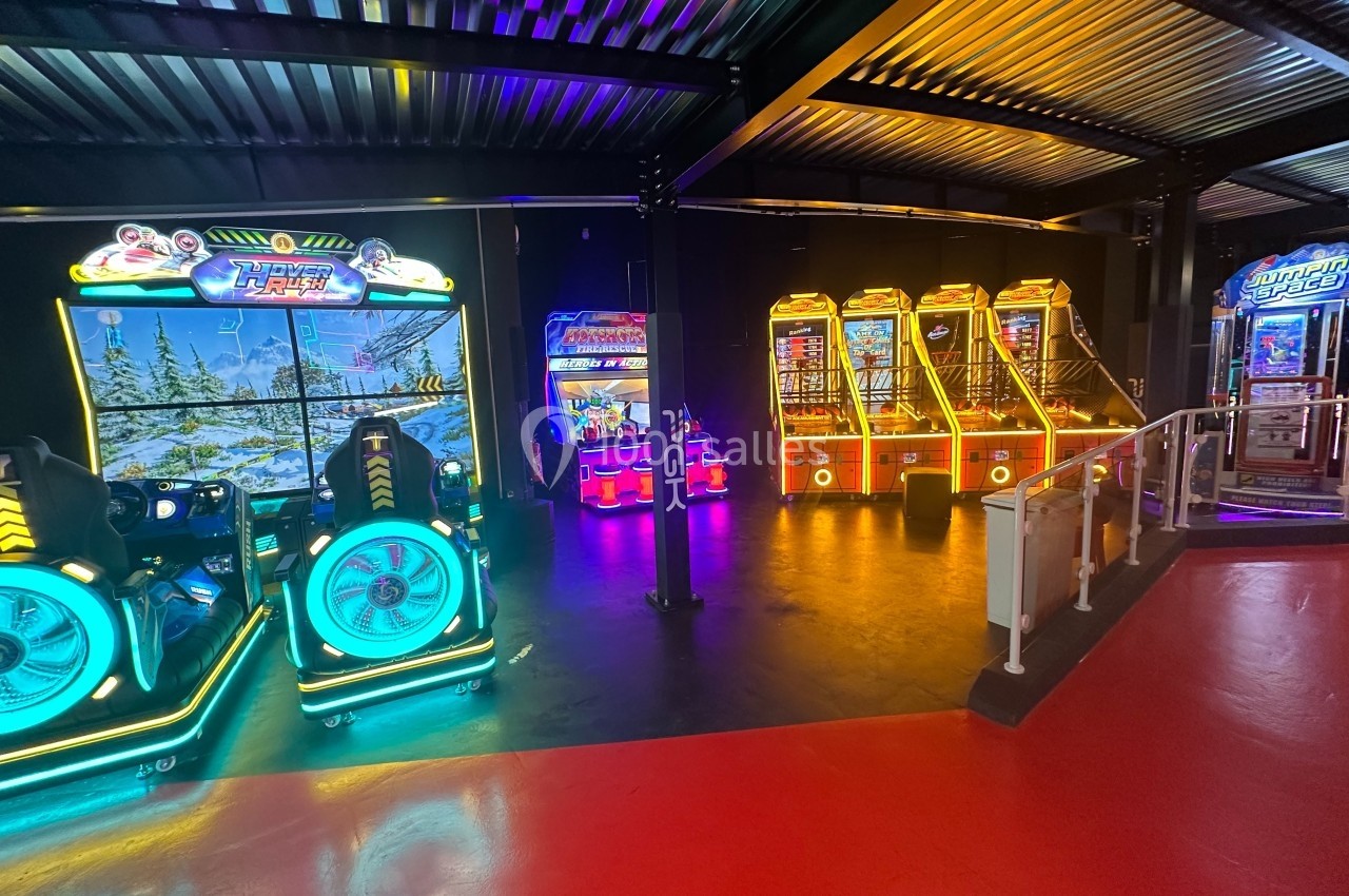 Salle d'arcade avec des bornes de jeux lumineuses et colorées alignées sous un éclairage tamisé.