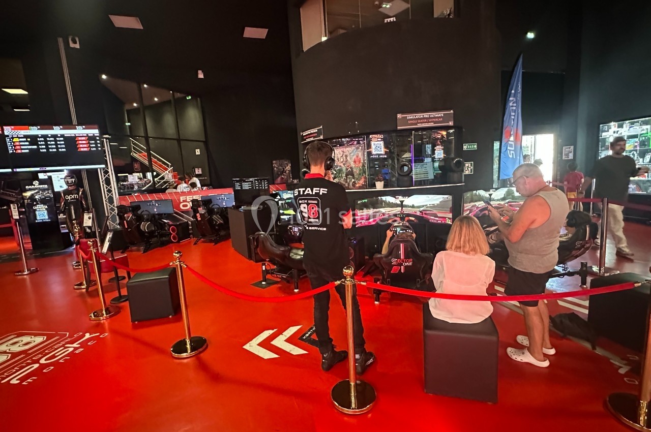 Des personnes observent des simulateurs de course automobile dans un espace intérieur avec un sol rouge et des écrans.