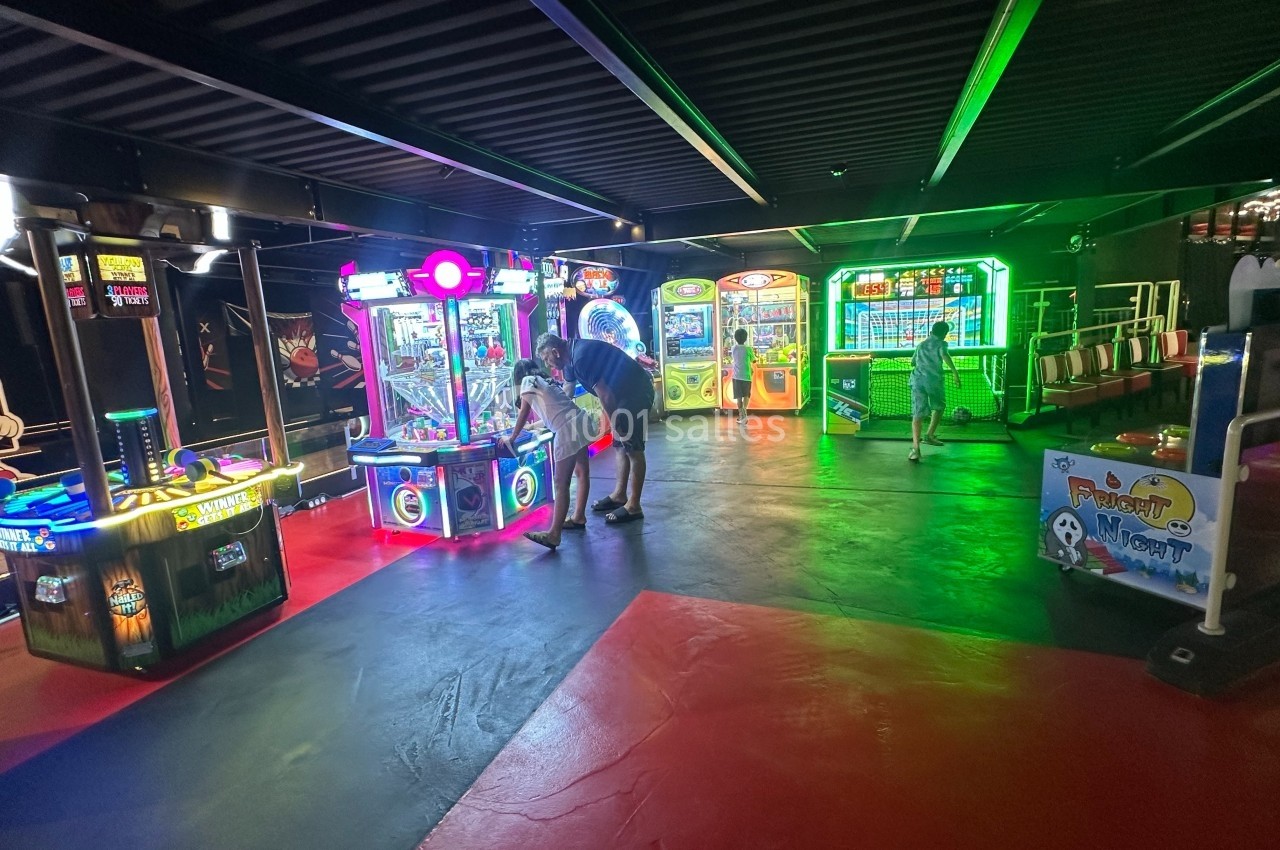 Salle d'arcade avec plusieurs machines de jeux lumineuses, un homme et une enfant interagissent avec les bornes.