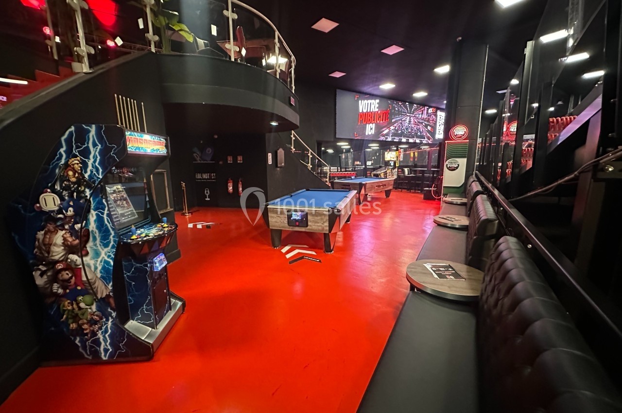 Salle de loisirs avec billard, borne d'arcade et banquettes, éclairée par des lumières rouges et noires.