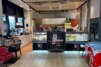 Intérieur d'une boutique avec comptoirs de vente proposant glaces, boissons et snacks, éclairée par des lumières modernes.