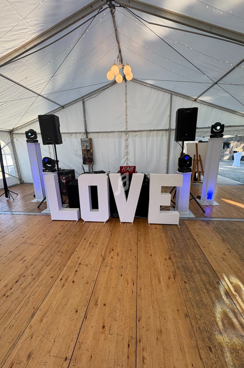 Lettres géantes formant le mot ’LOVE’ dans une tente décorée avec des lumières et un équipement de sonorisation.