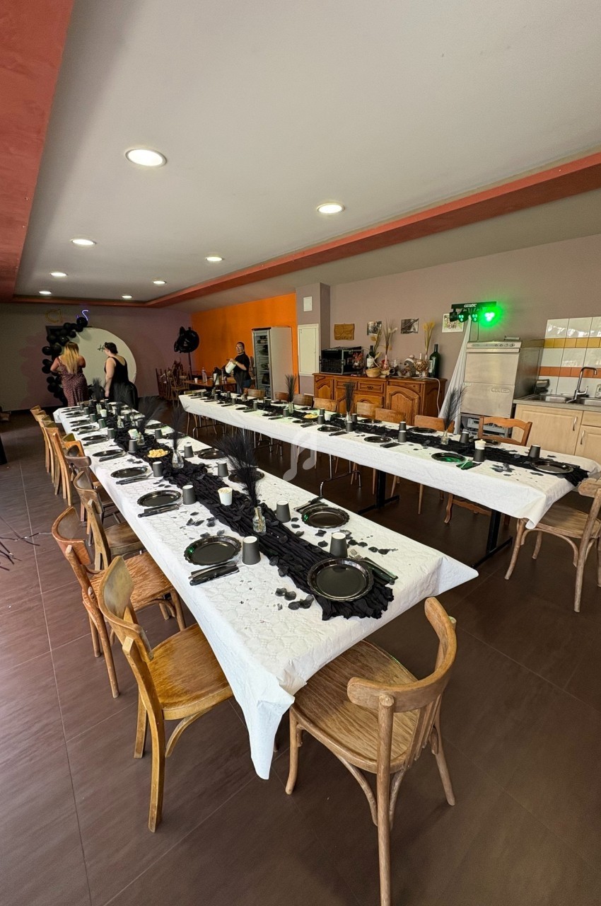 Salle décorée avec deux longues tables dressées avec vaisselle noire et nappes blanches, prête pour un événement.