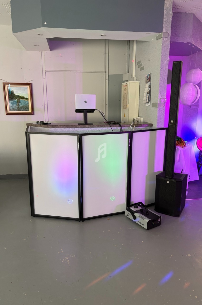 Console DJ avec panneaux lumineux, haut-parleur vertical et équipement audio dans une salle décorée.