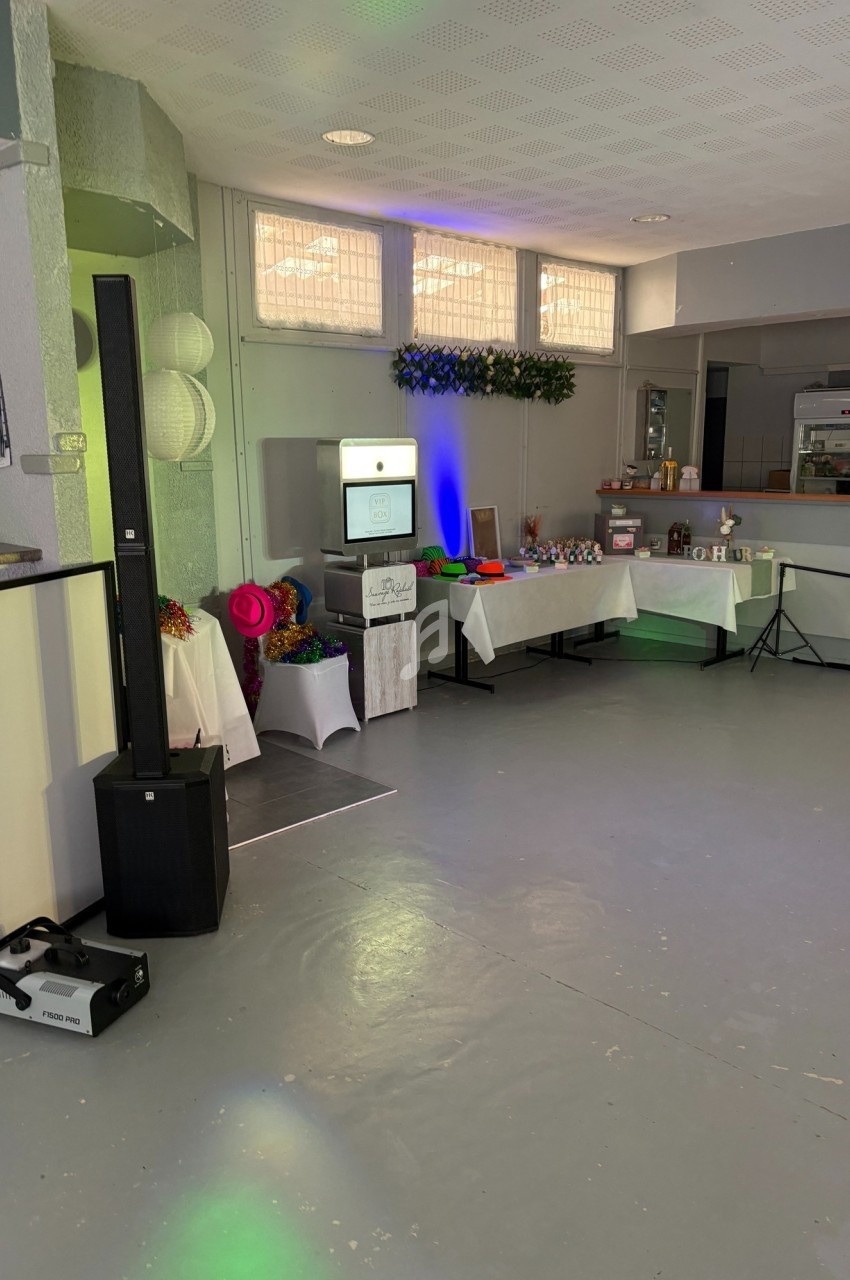 Salle décorée avec une borne photo, des accessoires colorés, des tables garnies et un éclairage d'ambiance.