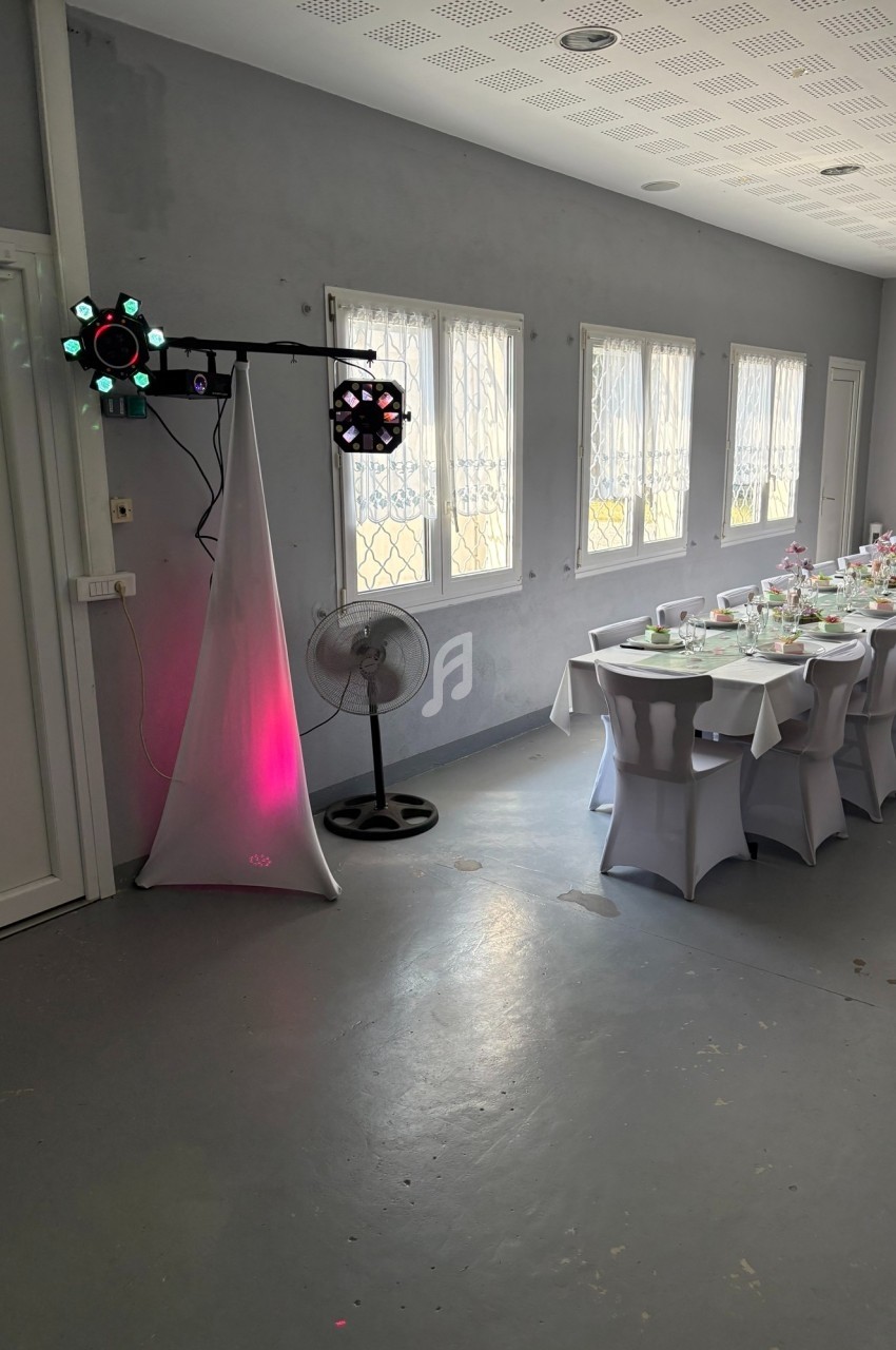 Salle décorée pour un événement avec une longue table dressée, des chaises blanches et un éclairage d'ambiance.