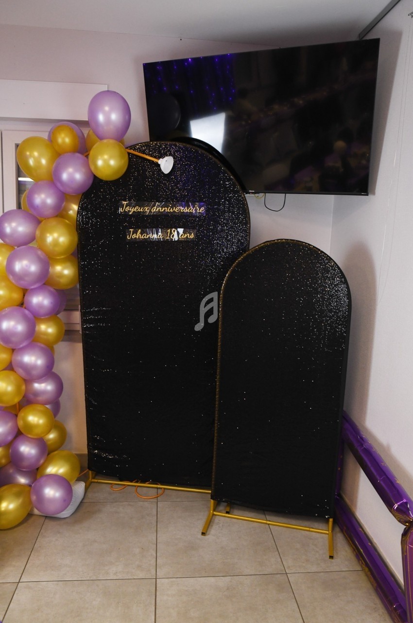 Mur décoratif noir scintillant avec ballons dorés et violets, et un message d'anniversaire lumineux.