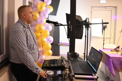 Un DJ mixe de la musique lors d'un événement festif, entouré de ballons jaunes et violets.