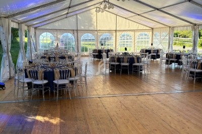 Intérieur d'une tente de réception avec tables rondes dressées, chaises transparentes et éclairage naturel.