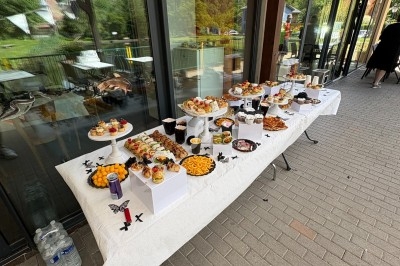 Table garnie de desserts variés et apéritifs, disposée en extérieur devant une baie vitrée avec vue sur la nature.