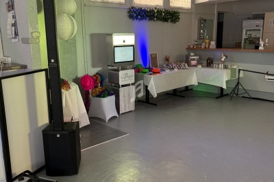 Salle décorée avec une borne photo, tables garnies d’accessoires colorés et un buffet en arrière-plan.