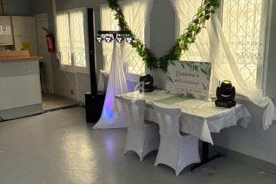 Salle décorée pour un événement avec guirlandes de fleurs, nappes blanches et matériel d'éclairage installé.