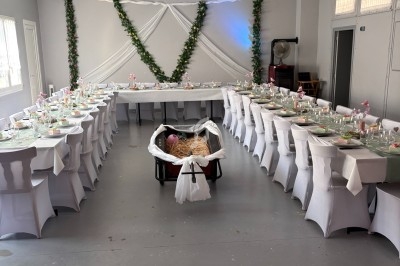 Salle décorée pour un événement avec tables dressées en U, nappes blanches et guirlandes de feuillage au mur.