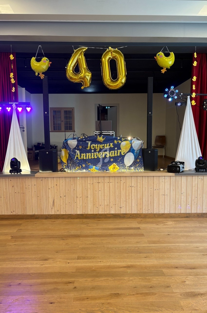Décoration de scène pour un 40e anniversaire avec ballons dorés, guirlandes et équipement de sonorisation.