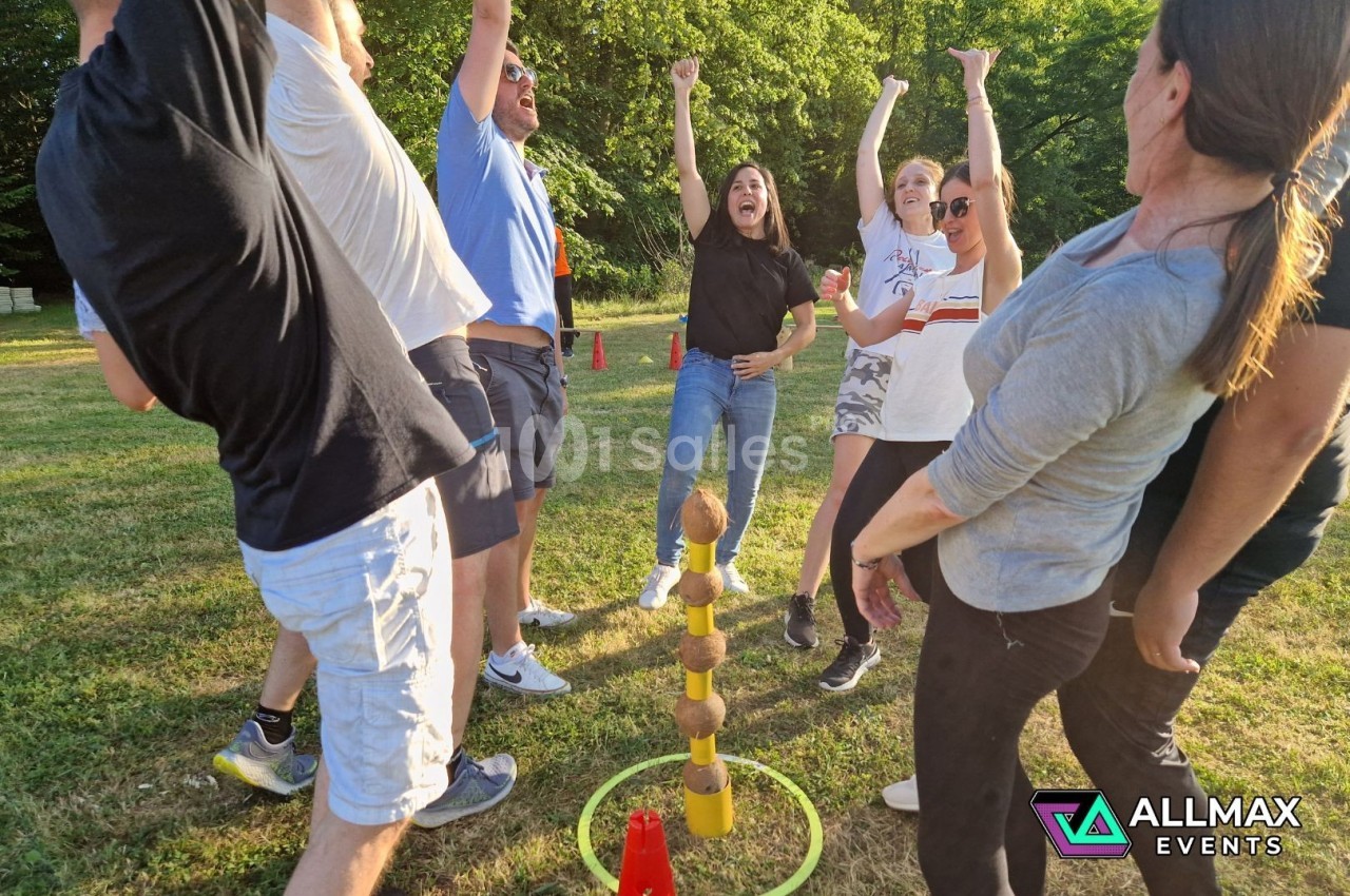 Un groupe de personnes célèbre autour d'un jeu d'adresse avec des noix de coco empilées sur une pelouse.