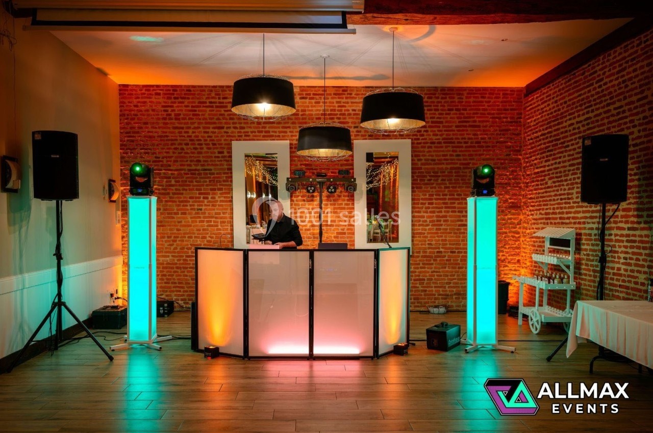 Poste de DJ éclairé avec des lumières colorées dans une salle au mur de briques, équipé de haut-parleurs et de décorations.