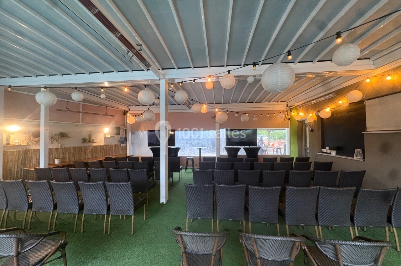 Salle de conférence en extérieur avec chaises noires alignées, décorations lumineuses et lanternes suspendues.