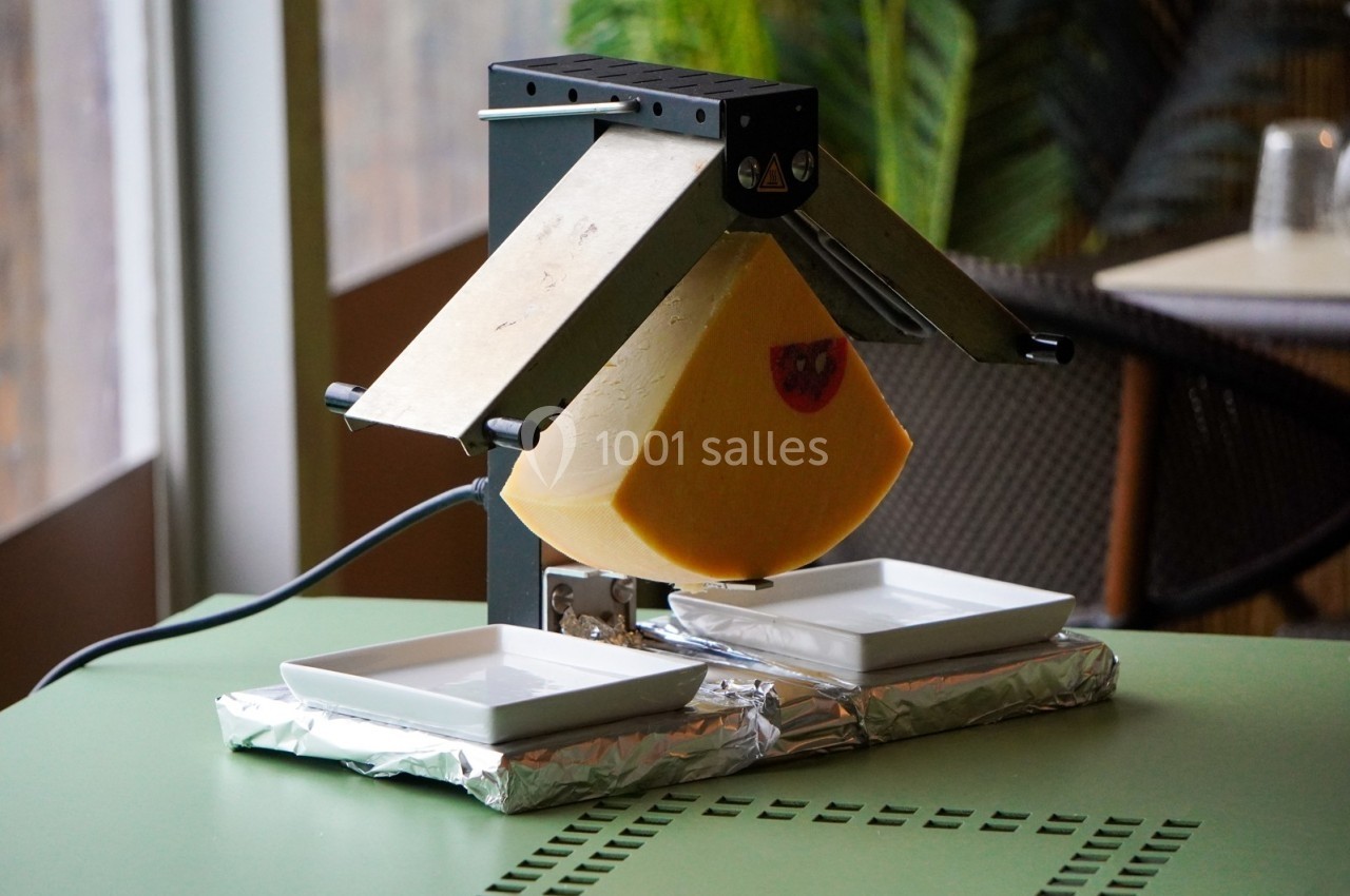 Appareil à raclette chauffant un demi-fromage, avec deux assiettes blanches placées en dessous pour recueillir le fromage…