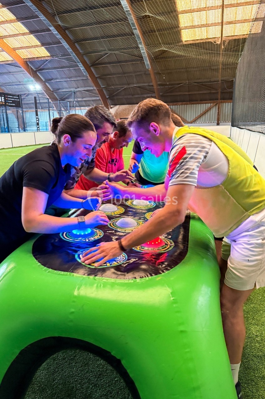 Des personnes s'affrontent autour d'un jeu interactif lumineux dans un espace sportif couvert.