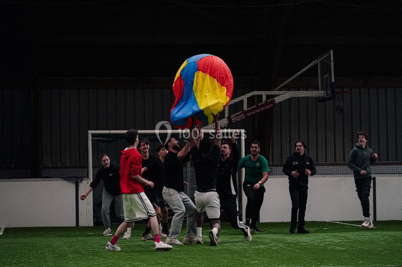 Des personnes jouent avec un ballon coloré dans un terrain couvert, entourées de filets et de murs.