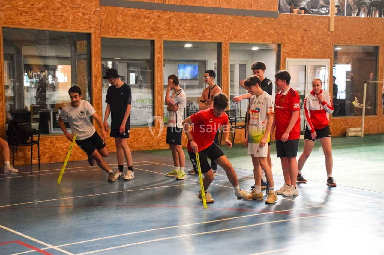 Des jeunes jouent à un jeu d'équipe avec des bâtons en plastique dans un gymnase lumineux.