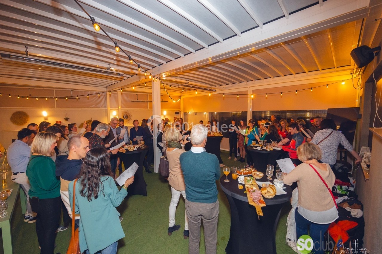 Groupe de personnes réunies dans une salle éclairée, discutant et partageant un buffet sur des tables hautes.
